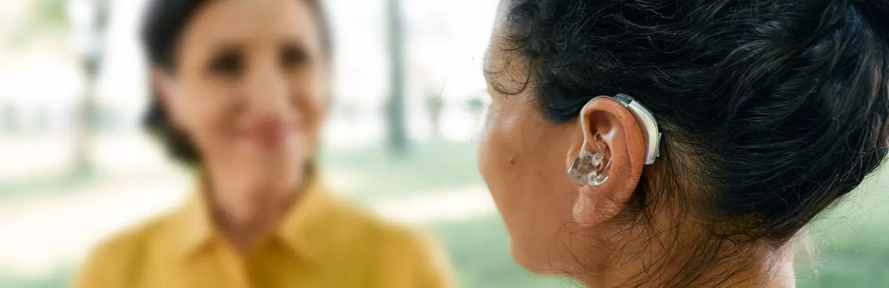 One woman with a hearing aid speaks with another woman outdoors