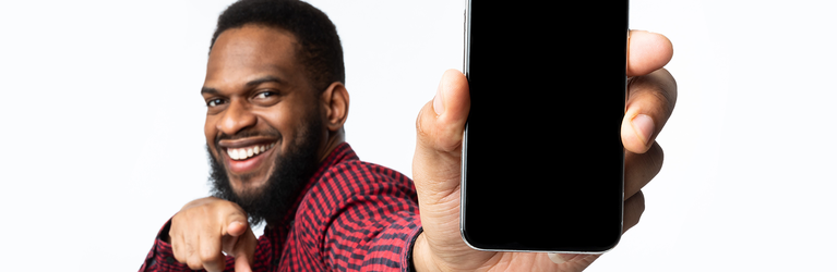 Dark skinned man holds a smart phone with a big smile and pointing at the camera