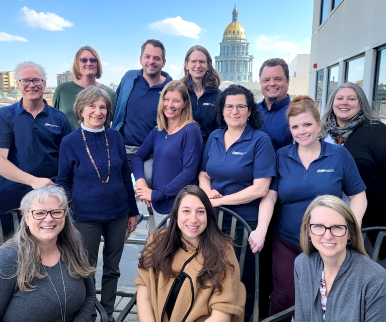 Colorado Commission for the Deaf, Hard of Hearing, and DeafBlind staff members pose outdoors with state capitol in background under a blue sky with clouds